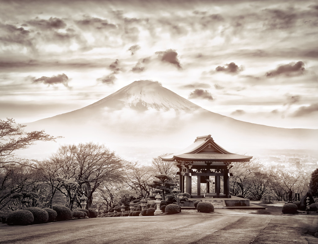 Sepia-toned photograph of a small Japanese shrine surrounded by barre trees and topiary bushes with Mt Fuji in the background