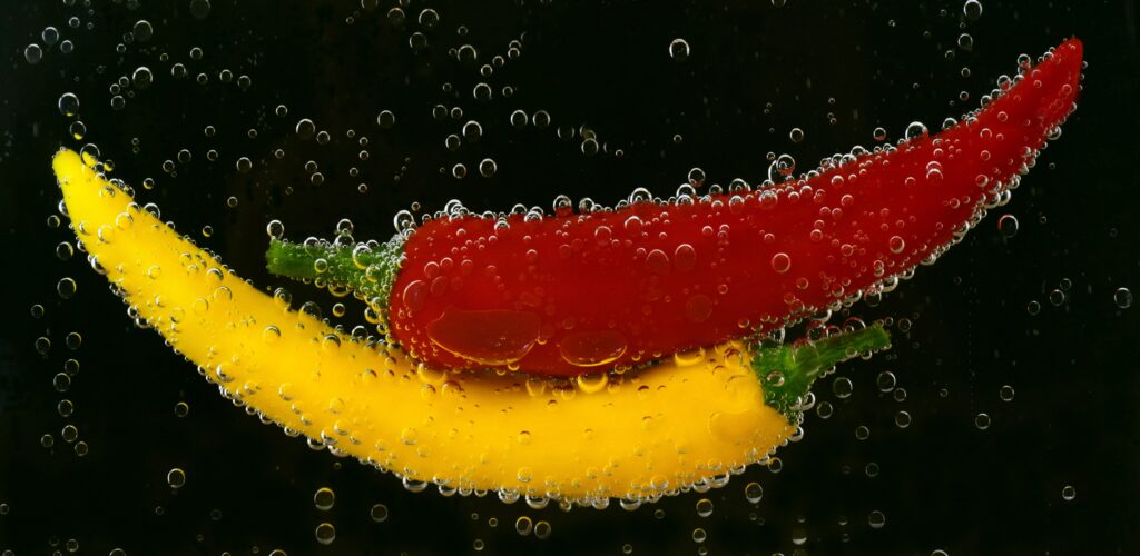 Depiction of two peppers, one red and one yellow, in water with water bubbles.
