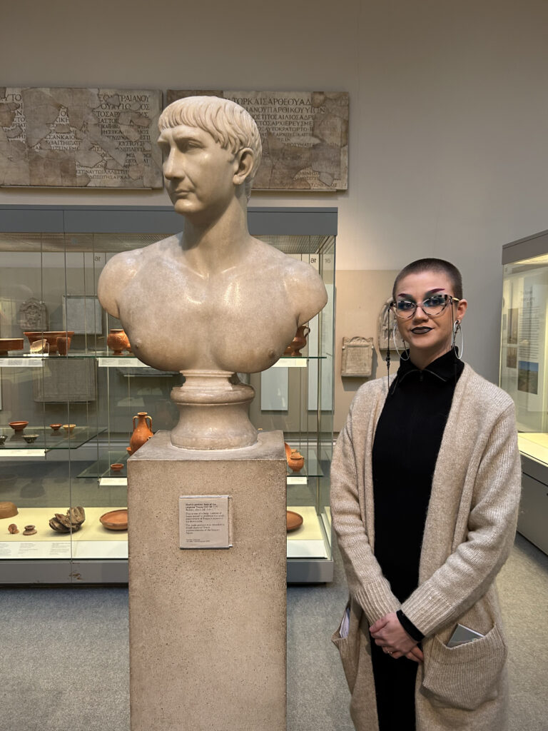 person standing next to marble bust of historic emperor of Rome Trajan