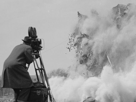 Black and white photo of 1940s camera operator filming building demolition