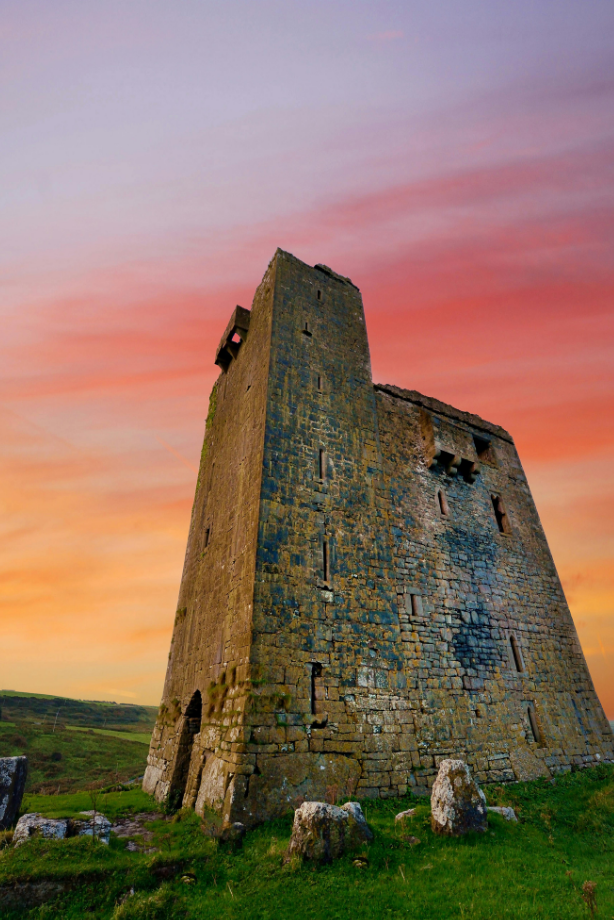 Photo: Tall, weathered stone tower standing in a grassy field under a colorful sunset sky.